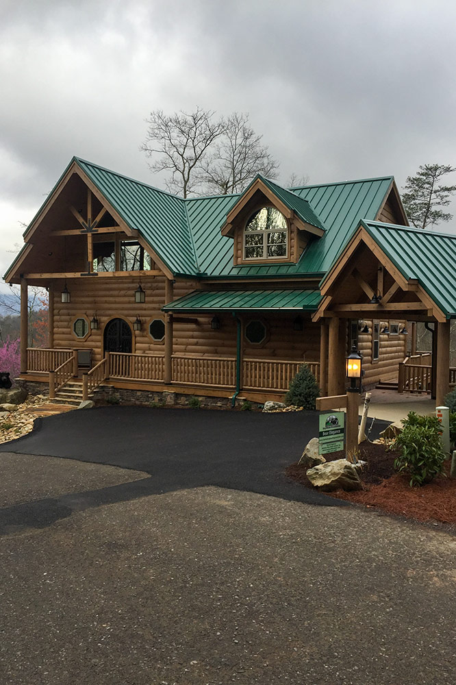 Large custom log cabin with green metal roof and covered porches