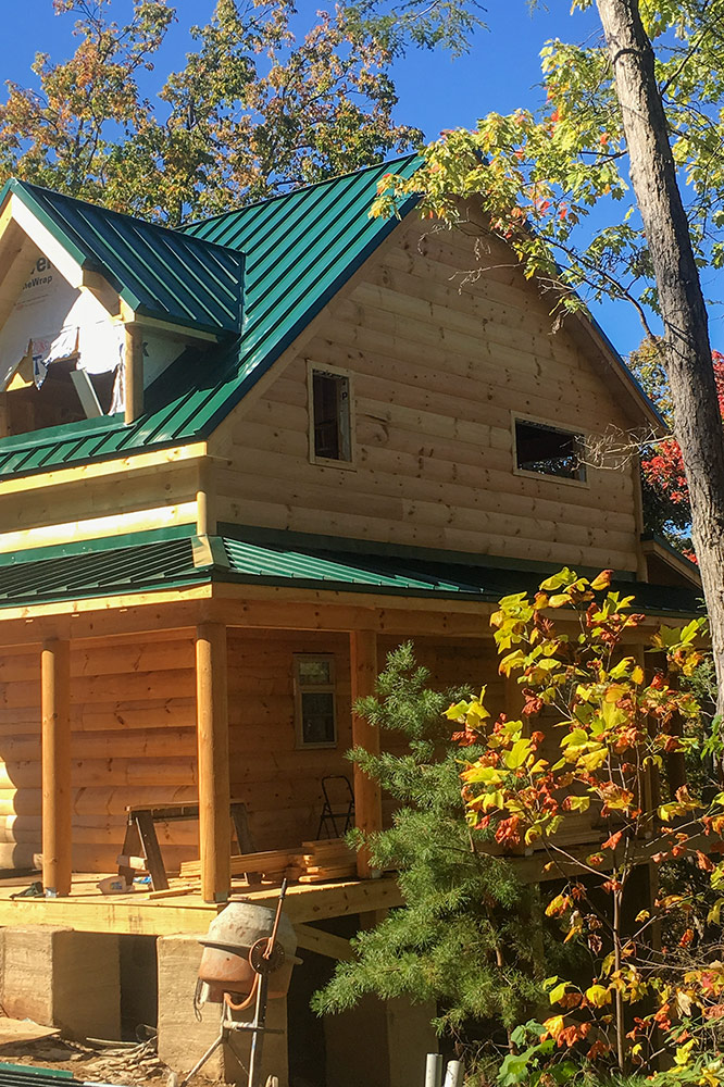 Custom log cabin with green metal roof surrounded by autumn foliage