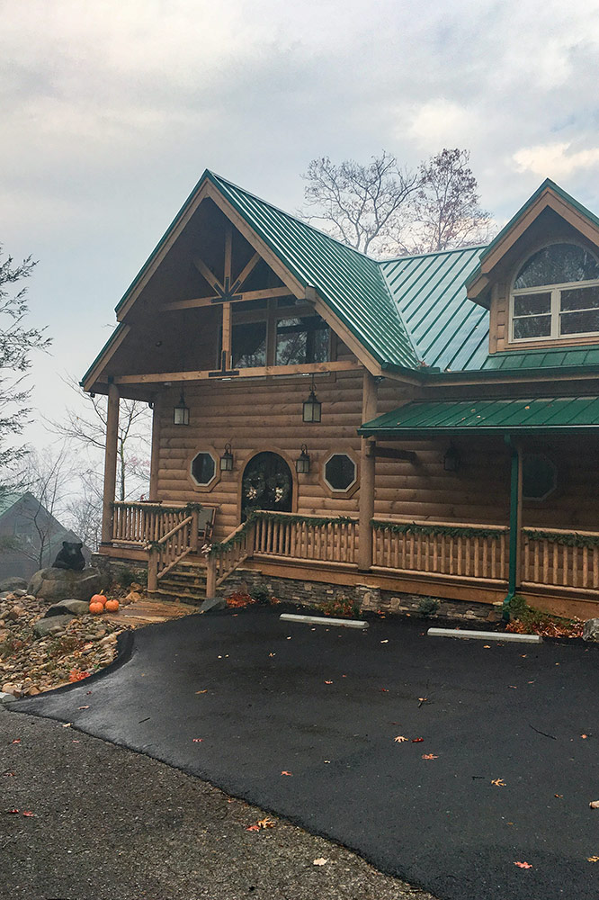 Custom cabin exterior with timber trusses, stone accents and green metal roof