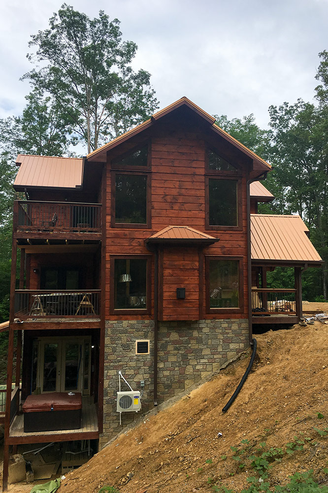 Three-story custom log cabin with covered decks and wooded surroundings
