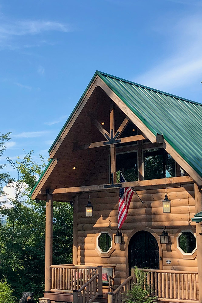 Custom log cabin entrance with timber posts, covered porch and green metal roof