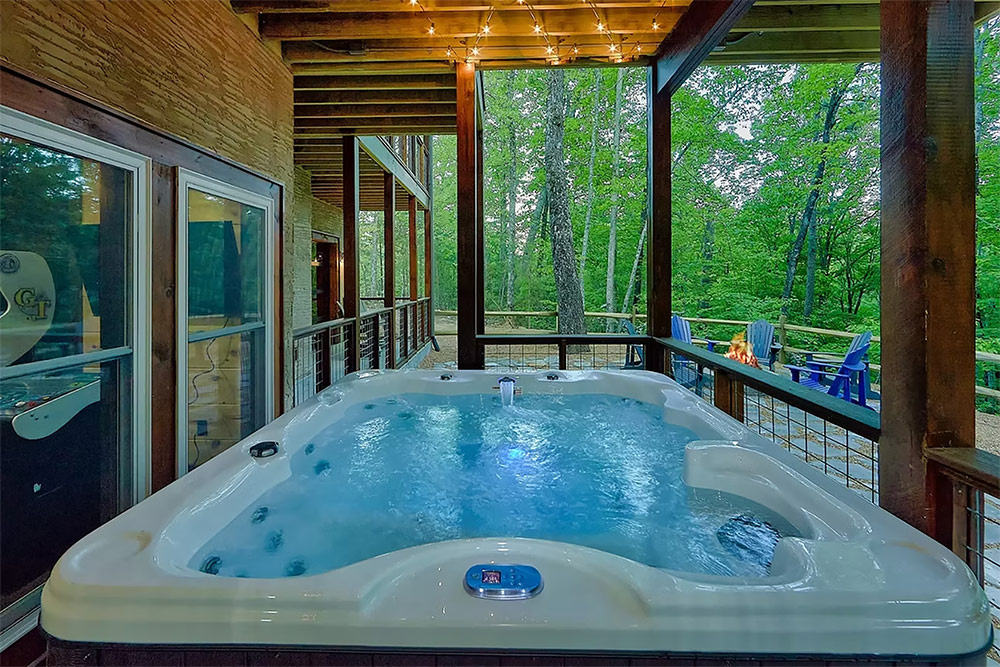 Covered deck featuring a private hot tub surrounded by trees